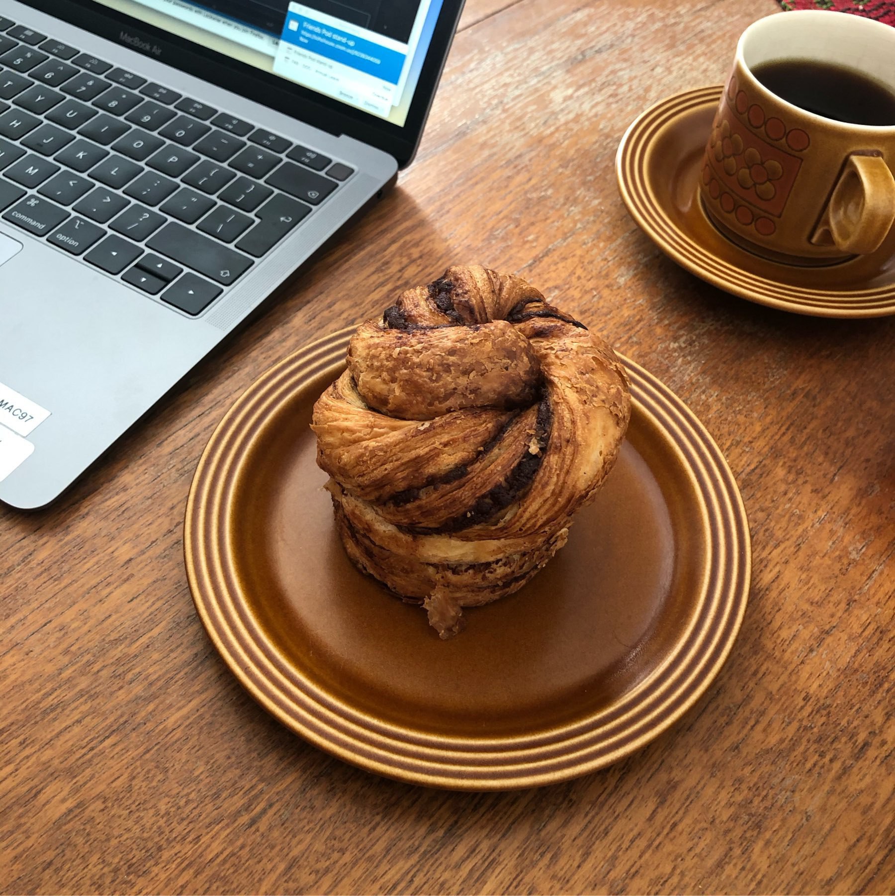 Cinnamon bun on a brown plate next to my MacBook Air and a nice cup of coffee.
