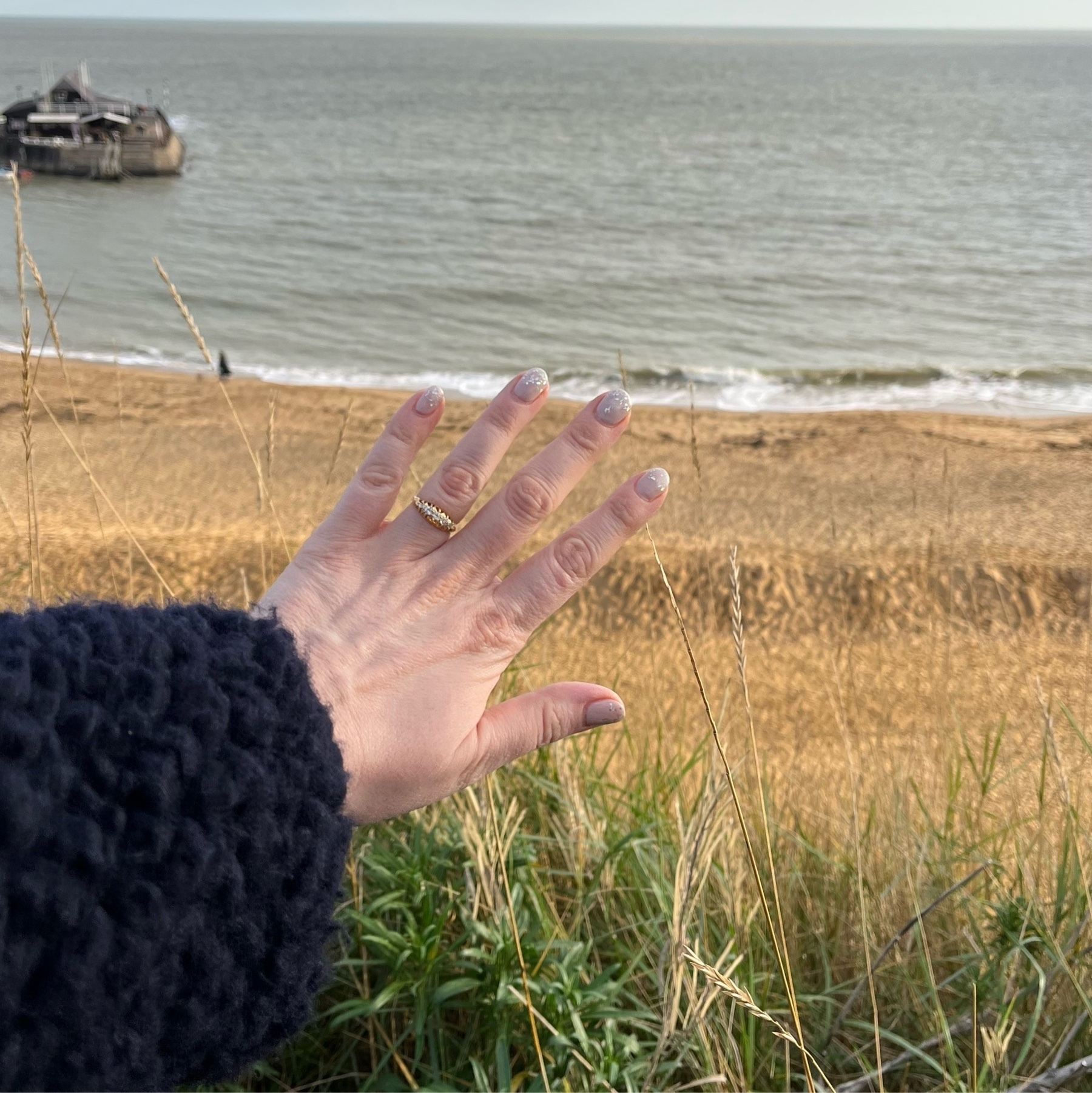 Hand wearing engagment ring against a sandy beach background